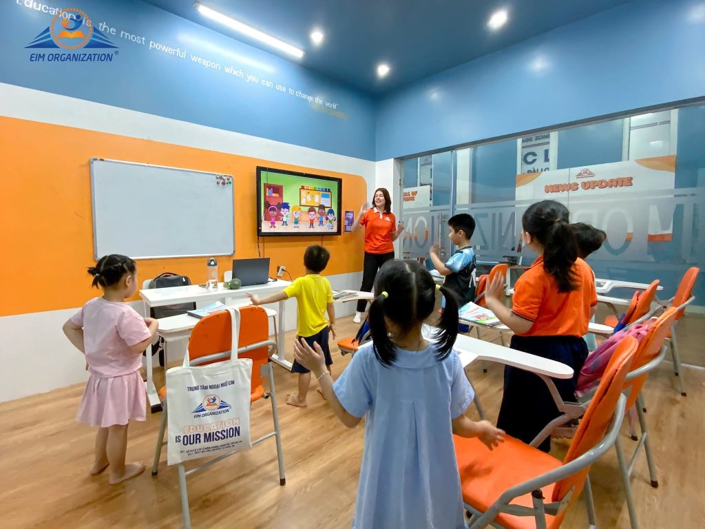 Có một thời điểm rất nhiều ba mẹ bắt đầu tìm kiếm cụm từ “Trung tâm tiếng Anh trẻ em Hải Phòng uy tín nhất”. Đó thường là khi con bắt đầu học tiếng Anh nghiêm túc hơn ở trường, chuẩn bị vào lớp 1, muốn cải thiện giao tiếp hoặc bắt đầu định hướng Cambridge. Nhưng có một vấn đề: “Uy tín nhất” không phải lúc nào cũng đồng nghĩa với “phù hợp nhất”. Một trung tâm có thể nổi tiếng nhưng chưa chắc phù hợp với độ tuổi, tính cách và mục tiêu học tập của con. Ngược lại, một chương trình ít quảng cáo hơn nhưng có sĩ số lớp phù hợp, giáo viên sát sao và lộ trình rõ ràng lại có thể mang đến trải nghiệm học tập tốt hơn. Vì vậy, thay vì chỉ tìm trung tâm tiếng Anh trẻ em Hải Phòng uy tín nhất, ba mẹ nên biết cách đánh giá một trung tâm thực sự tốt cho con. Dưới đây là 7 tiêu chí quan trọng có thể giúp ba mẹ lựa chọn dễ dàng hơn. Thế nào là một trung tâm tiếng Anh trẻ em uy tín? Một trung tâm tiếng Anh trẻ em Hải Phòng uy tín nhất không nên được đánh giá chỉ bằng số năm hoạt động, số lượng học viên hay những lời quảng cáo như “chuẩn quốc tế”. Với trẻ em, chất lượng đào tạo nằm ở nhiều yếu tố kết hợp: Đúng độ tuổi → đúng phương pháp → đúng môi trường → đúng lộ trình → đúng cách đánh giá. Một bé 4 tuổi sẽ không thể học theo cách của học sinh lớp 5. Một học sinh lớp 5 đang chuẩn bị Cambridge cũng không nên học giống một bạn mới bắt đầu làm quen với tiếng Anh. Ngay cả trong hệ thống Cambridge English dành cho trẻ em, các mốc Pre A1 Starters, A1 Movers và A2 Flyers cũng được thiết kế theo từng mức độ phát triển ngôn ngữ. Cambridge mô tả Starters, Movers và Flyers là các chứng chỉ dành cho học sinh nhỏ tuổi, giúp trẻ phát triển Listening, Speaking, Reading và Writing theo từng bước. Do đó, lộ trình phù hợp với từng giai đoạn quan trọng không kém việc lựa chọn giáo viên. 7 tiêu chí đánh giá trung tâm tiếng Anh trẻ em Hải Phòng uy tín nhất 1. Chương trình học phải phù hợp với từng độ tuổi Một trong những sai lầm phổ biến khi học tiếng Anh cho bé tại Hải Phòng là phụ huynh quá chú trọng việc con phải học được thật nhiều từ vựng và ngữ pháp. Nhưng trẻ nhỏ không học ngôn ngữ giống người lớn. Với trẻ mầm non, việc học cần gắn với hình ảnh, âm thanh, vận động, trò chơi, câu chuyện và những tình huống gần gũi. Khi lên tiểu học, trẻ có thể từng bước phát triển: Từ vựng theo chủ đề. Cấu trúc câu. Đọc hiểu. Viết câu. Phản xạ giao tiếp. Khả năng trình bày. Đến THCS, chương trình có thể tăng dần tính học thuật và yêu cầu cao hơn về ngữ pháp, đọc hiểu, viết và tư duy bằng tiếng Anh. Vì vậy, khi tìm Trung tâm tiếng Anh trẻ em Hải Phòng uy tín nhất, ba mẹ nên xem trung tâm có chia chương trình theo độ tuổi hay chỉ sử dụng một phương pháp chung cho tất cả học sinh. Xem thêm: Tiếng Anh mẫu giáo Hải Phòng 100% giáo viên nước ngoài 2. Giáo viên không chỉ cần giỏi tiếng Anh mà phải biết cách dạy trẻ Một người nói tiếng Anh tốt chưa chắc là một giáo viên trẻ em tốt. Trẻ 4 tuổi cần một cách tiếp cận hoàn toàn khác trẻ 10 tuổi. Giáo viên cần biết cách tạo tương tác, khuyến khích trẻ nói, xử lý khi trẻ mất tập trung và biến kiến thức thành hoạt động mà trẻ muốn tham gia. Đây cũng là lý do mô hình Tiếng Anh trẻ em 100% giáo viên bản ngữ được nhiều phụ huynh quan tâm. Khi học với giáo viên nước ngoài, trẻ có thêm cơ hội tiếp xúc với tiếng Anh trong ngữ cảnh giao tiếp tự nhiên. Thay vì chỉ học: “What is this?” trên sách, trẻ có thể phải nghe câu hỏi, quan sát tình huống và phản hồi trực tiếp. Tuy nhiên, 100% giáo viên nước ngoài không nên được xem là tiêu chí duy nhất. Một chương trình tốt vẫn cần giáo viên có phương pháp sư phạm phù hợp với trẻ và có sự hỗ trợ khi học sinh gặp khó khăn. 3. Lớp học đủ nhỏ để giáo viên thực sự nhìn thấy từng học sinh Hãy thử tưởng tượng một lớp có quá nhiều học sinh. Trong 90 phút, giáo viên phải: Giảng bài. Quản lý lớp. Tổ chức hoạt động. Kiểm tra bài. Sửa phát âm. Hỗ trợ từng học sinh. Điều này khiến thời gian dành cho từng trẻ bị thu hẹp. Đặc biệt với ngoại ngữ, việc được nói và được sửa có ý nghĩa rất lớn. Một bé phát âm sai một âm nhưng không được phát hiện có thể tiếp tục lặp lại lỗi đó trong thời gian dài. Vì vậy, khi tìm trung tâm tiếng Anh trẻ em Hải Phòng uy tín nhất, sĩ số lớp cũng là một tiêu chí đáng quan tâm. Không phải lớp càng ít học sinh thì chắc chắn càng tốt, nhưng lớp học cần đủ quy mô để giáo viên có thể quan sát và hỗ trợ từng trẻ. Tại EIM, mô hình lớp học được định hướng ở quy mô khoảng 8–12 học sinh, tạo điều kiện để trẻ có nhiều cơ hội tương tác với giáo viên và bạn bè. Xem thêm: Review Trung Tâm Tiếng Anh Mầm Non Hải Phòng Uy Tín Được Nhiều Phụ Huynh Lựa Chọn 4. Chương trình cần có lộ trình, không phải học “mỗi buổi một chủ đề” Một vấn đề phụ huynh thường khó nhận ra là: Con đi học đều nhưng không biết mình đang đi đến đâu. Tuần này học màu sắc. Tuần sau học động vật. Tuần sau nữa học gia đình. Trẻ vẫn học được từ mới nhưng nếu các nội dung không được kết nối thành một hệ thống, kiến thức rất dễ rời rạc. Một trung tâm tiếng Anh trẻ em Hải Phòng uy tín nhất cần giúp phụ huynh nhìn thấy lộ trình: Con đang ở đâu → đang học gì → cần đạt gì → bước tiếp theo là gì. Ví dụ, với chương trình Cambridge dành cho trẻ, ba mẹ có thể hình dung các mốc: Pre A1 Starters → A1 Movers → A2 Flyers. Cambridge xác định Starters là mốc đầu tiên, Movers là bước tiếp theo và Flyers là cấp độ cuối trong nhóm chứng chỉ Young Learners. Các bài thi được xây dựng xoay quanh những tình huống quen thuộc và đánh giá cả bốn kỹ năng. Như vậy, chứng chỉ không nên được xem là mục tiêu duy nhất. Nó có thể trở thành một cột mốc để đo quá trình phát triển tiếng Anh của trẻ. 5. Đừng chỉ dạy trẻ “làm bài” – hãy cho trẻ sử dụng tiếng Anh Đây là điểm tạo nên khác biệt giữa học tiếng Anh cho bé tại Hải Phòng và thực sự sử dụng tiếng Anh. Một bé có thể biết: “Apple nghĩa là quả táo.” Nhưng nếu giáo viên hỏi: “What fruit do you like?” bé có thể không biết trả lời. Đó là khoảng cách giữa kiến thức thụ động và khả năng sử dụng ngôn ngữ. Một môi trường học tốt cần tạo cơ hội để trẻ: Nghe tiếng Anh. Trả lời câu hỏi. Hỏi lại người khác. Mô tả sự vật. Kể chuyện. Thảo luận. Thuyết trình. Làm việc nhóm. Mục tiêu cuối cùng là hình thành phản xạ giao tiếp tự nhiên, thay vì chỉ ghi nhớ câu trả lời. Xem thêm: Học Tiếng Anh Cho Trẻ Mầm Non Tại Hải Phòng – Nền Tảng Vững Vàng Cho Tương Lai Cùng EIM 6. Giáo trình cũng quyết định rất lớn đến trải nghiệm học tập Một chương trình dành cho trẻ em không nên chỉ có textbook và worksheet. Trẻ cần được tiếp cận tiếng Anh thông qua những chủ đề khiến chúng tò mò về thế giới. Đó là lý do giáo trình National Geographic Learning là một hướng tiếp cận đáng chú ý. Thay vì học ngôn ngữ tách biệt với kiến thức, trẻ có thể tiếp xúc với các chủ đề về: Động vật. Thiên nhiên. Khoa học. Con người. Văn hóa. Môi trường. Thế giới xung quanh. Cách tiếp cận này giúp tiếng Anh trở thành công cụ để khám phá kiến thức, thay vì chỉ là một môn học. Với những phụ huynh đang tìm Giáo trình National Geographic Learning, điều quan trọng không chỉ là tên giáo trình mà còn là cách giáo viên khai thác nội dung trong lớp. Cùng một bộ tài liệu, nhưng cách tổ chức hoạt động khác nhau có thể tạo ra trải nghiệm học tập hoàn toàn khác. 7. Phụ huynh phải nhìn thấy sự tiến bộ của con Một trung tâm tiếng Anh trẻ em Hải Phòng uy tín nhất không nên để phụ huynh phải đoán xem con có tiến bộ hay không. Ba mẹ cần được biết: Con đang mạnh ở đâu? Con đang yếu ở đâu? Con đã cải thiện điều gì? Giai đoạn tiếp theo cần tập trung vào đâu? Có thể theo dõi tiến bộ thông qua: Tiêu chí Điều phụ huynh có thể quan sát Listening Con hiểu yêu cầu bằng tiếng Anh tốt hơn Speaking Con chủ động trả lời và diễn đạt dài hơn Pronunciation Con phát âm rõ và chính xác hơn Vocabulary Con sử dụng từ trong ngữ cảnh thay vì chỉ nhớ nghĩa Reading Con hiểu nội dung thay vì chỉ đọc từng từ Writing Con viết được câu và đoạn văn có cấu trúc Đây mới là những dấu hiệu thực tế để đánh giá hiệu quả của việc học. EIM – môi trường học tiếng Anh cho trẻ từ 3–15 tuổi Nếu ba mẹ đang tìm trung tâm tiếng Anh trẻ em Hải Phòng uy tín nhất, EIM có thể là một lựa chọn đáng tham khảo cho trẻ trong độ tuổi 3–15 tuổi. Chương trình được định hướng theo từng giai đoạn phát triển của trẻ, từ Tiếng Anh mầm non Hải Phòng, Tiếng Anh tiểu học Hải Phòng đến chương trình dành cho học sinh THCS. Một số điểm nổi bật của môi trường học tập tại EIM: 100% giáo viên nước ngoài. Trợ giảng Việt Nam hỗ trợ học sinh. Lớp học quy mô khoảng 8–12 học sinh. Nội dung học tập gắn với giáo trình National Geographic Learning. Định hướng chương trình tiếng Anh chuẩn Cambridge. Tập trung phát triển giao tiếp, phát âm và 4 kỹ năng. Có lộ trình phù hợp với từng độ tuổi. Với trẻ nhỏ, mục tiêu không phải là ép con học thật nhiều. Điều quan trọng hơn là giúp con không sợ tiếng Anh, thích sử dụng tiếng Anh và từng bước sử dụng tiếng Anh một cách tự nhiên. Nếu ba mẹ đang tìm Trung tâm tiếng Anh trẻ em Hải Phòng cho con từ 3–15 tuổi, hãy liên hệ 0917 599 729 để đăng ký học thử tiếng Anh miễn phí cho bé. Đây là cơ hội để ba mẹ trực tiếp quan sát môi trường học tập, cách giáo viên tương tác với trẻ và tìm hiểu lộ trình phù hợp trước khi đưa ra quyết định. Xem thêm: Học Tiếng Anh Cho Bé Tại Hải Phòng: Vì Sao Môi Trường Tự Nhiên Quan Trọng Hơn “Học Thuộc”? Trung Tâm Tiếng Anh Cho Bé 3-5 Tuổi Tại Hải Phòng – Khởi Đầu Sớm, Tự Tin Giao Tiếp Tương Lai 